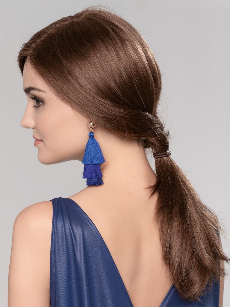 A woman with brown hair styled in a ponytail, wearing a blue tassel earring, and a blue dress, shown from the side.